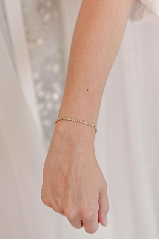 Bride wearing a dainty stainless steel gold plated tennis bracelet with 2mm cubic zirconia.