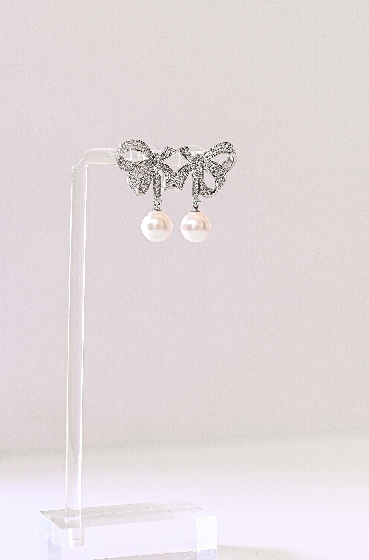 A pair of silver bow-shaped stud bridal earrings with dangling white pearls.