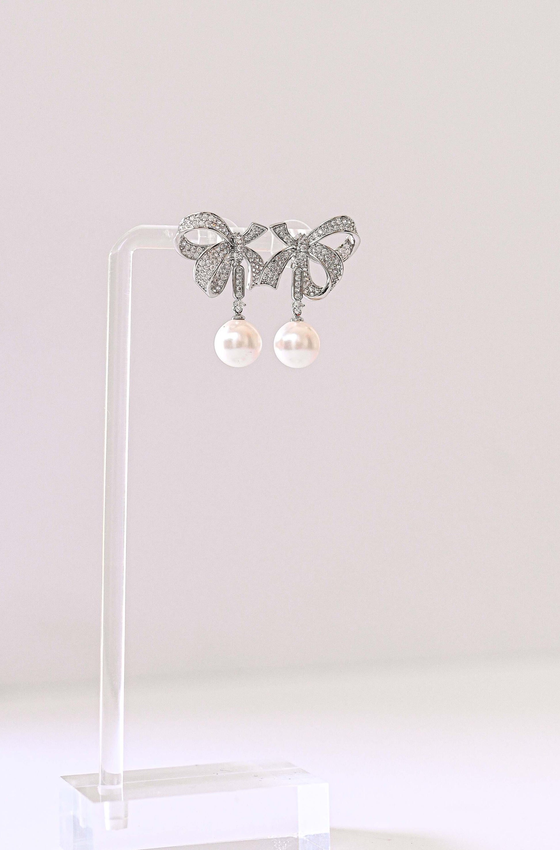 A pair of silver bow-shaped stud bridal earrings with dangling white pearls.