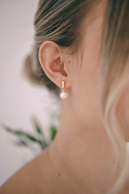 Bride wearing a gold earring with cubic zirconia and a faux pearl